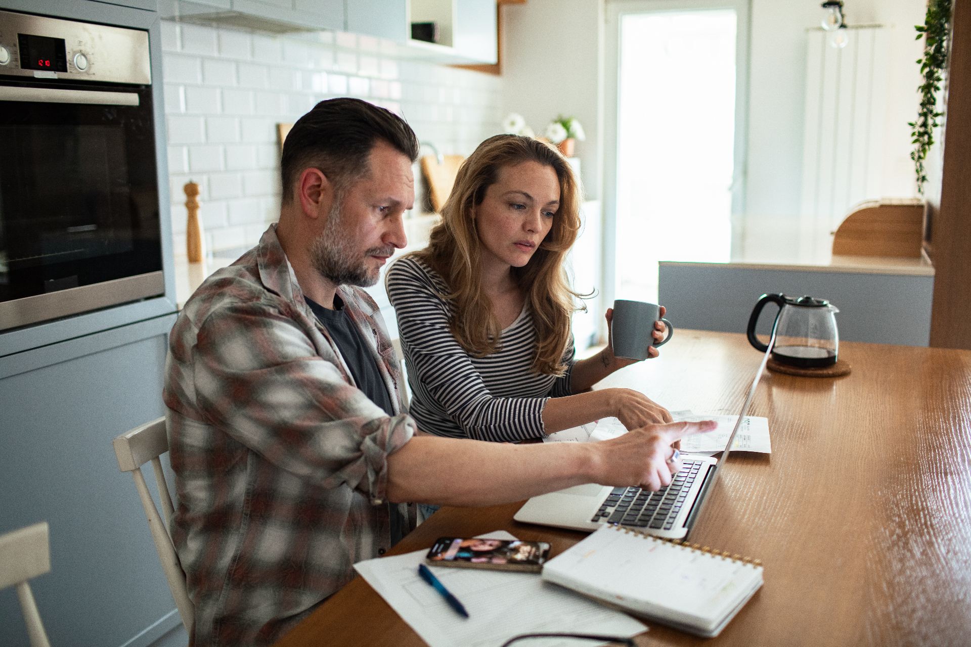A couple at their kitchen table going over bills on a laptop.
